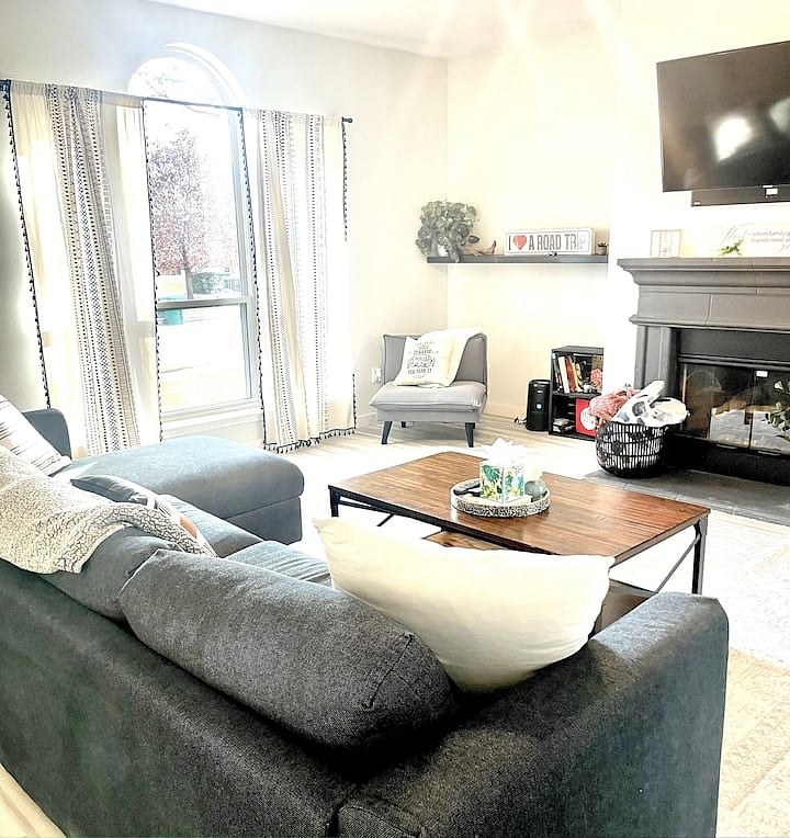 Bright living room with a gray sectional, wood coffee table, wall-mounted TV, and an arched window