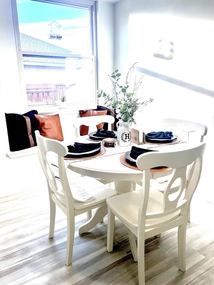 Round white dining table set for four by a sunny window seat